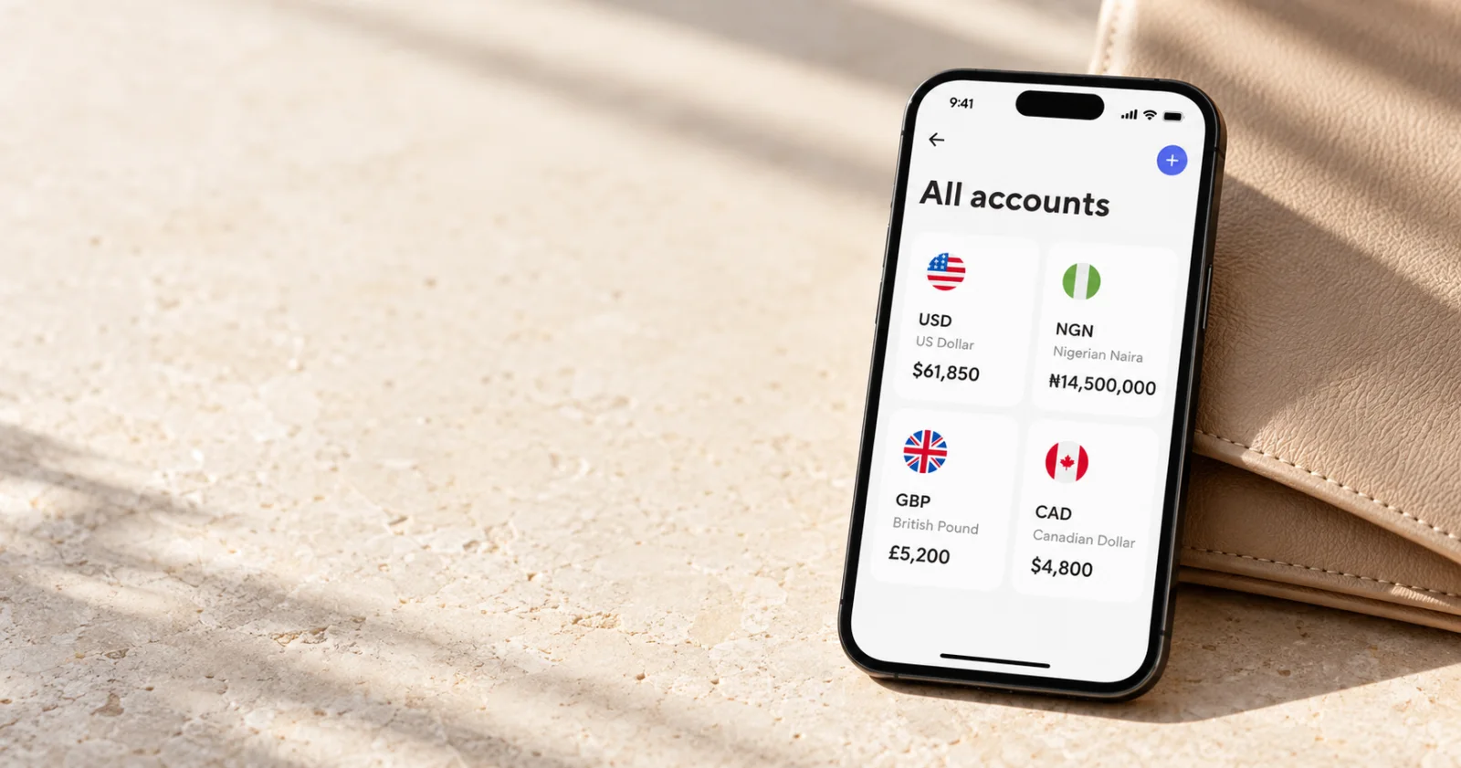 A phone showing separate US dollar, naira, pound and Canadian dollar balances on warm limestone.